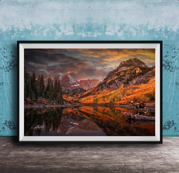 The image is a framed photograph depicting a serene mountain landscape with a lake, trees, and mountains in the background, reflecting the vibrant colors of the sky.