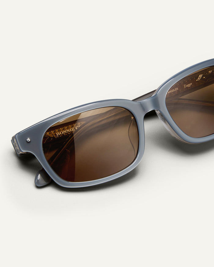 Detail shot of Bonnie Clyde Dagger sunglasses in layered silver with brown lenses.