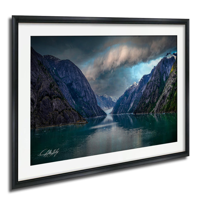 a serene mountain landscape with a calm lake in the foreground, surrounded by towering, snow-capped peaks under a dramatic cloudy sky.