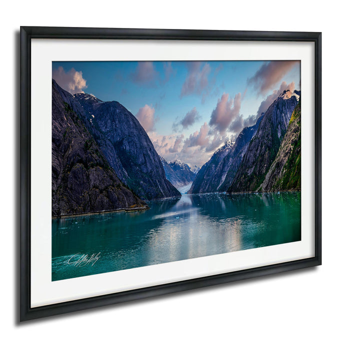 a serene mountain landscape with a calm lake in the foreground, surrounded by towering, snow-capped peaks under a picturesque blue sky with wispy clouds.