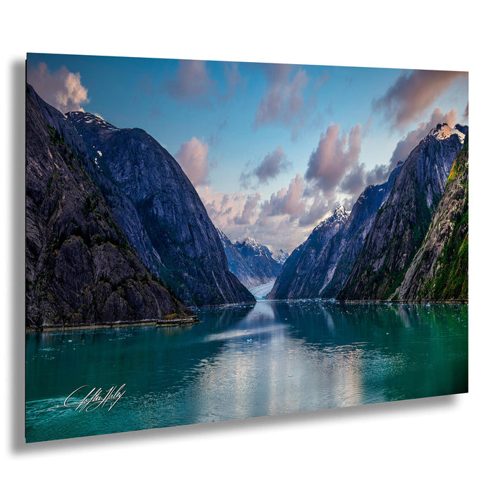a serene landscape with a large body of water surrounded by towering mountains, with a clear blue sky and fluffy white clouds above.