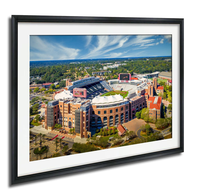 The image is an aerial view of a large sports stadium with multiple buildings surrounding it, including a large stadium with a red roof and a smaller building with a red roof.