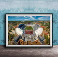 The image is an aerial view of a large sports stadium with a football field, surrounded by buildings and a blue sky.