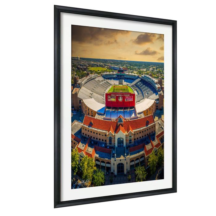 An aerial view of a large stadium with a red roof and a large sign on top, surrounded by a cityscape.