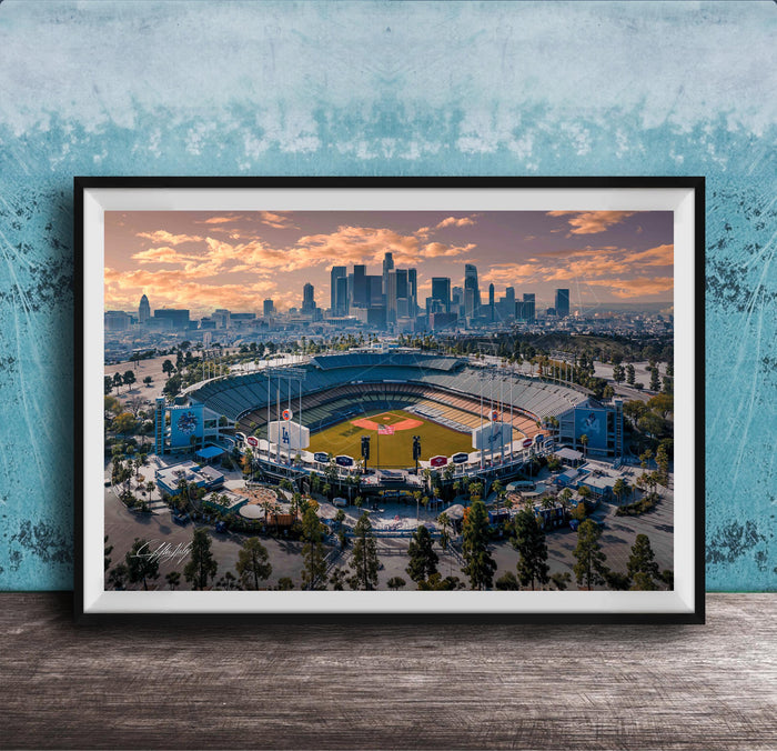 An aerial view of a baseball stadium with the city skyline in the background, framed in a black frame and displayed on a wooden surface.