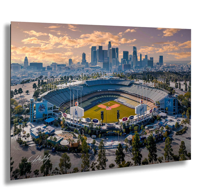 An aerial view of a baseball stadium with the city skyline in the background, set against a colorful sunset sky.