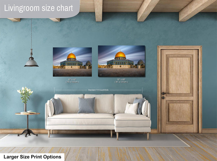 a living room with a white sofa and a wooden door. Above the sofa, there are two framed photographs of the Dome of the Rock, a significant landmark in Jerusalem. The photographs are of different sizes, with one being larger than the other. The living room has a blue wall and a wooden floor, creating a cozy and inviting atmosphere.