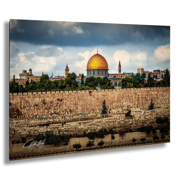 the Dome of the Rock, a prominent landmark in Jerusalem, Israel. The golden dome of the mosque stands out against the cloudy sky, surrounded by lush greenery and the city's historic buildings.