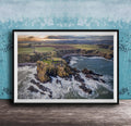 The image is a framed aerial view of a coastal landscape, featuring a rocky outcrop, a small island, and the ocean.