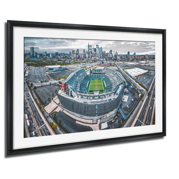 An aerial view of a large sports stadium surrounded by a city skyline, with the stadium's field and surrounding parking lots visible.