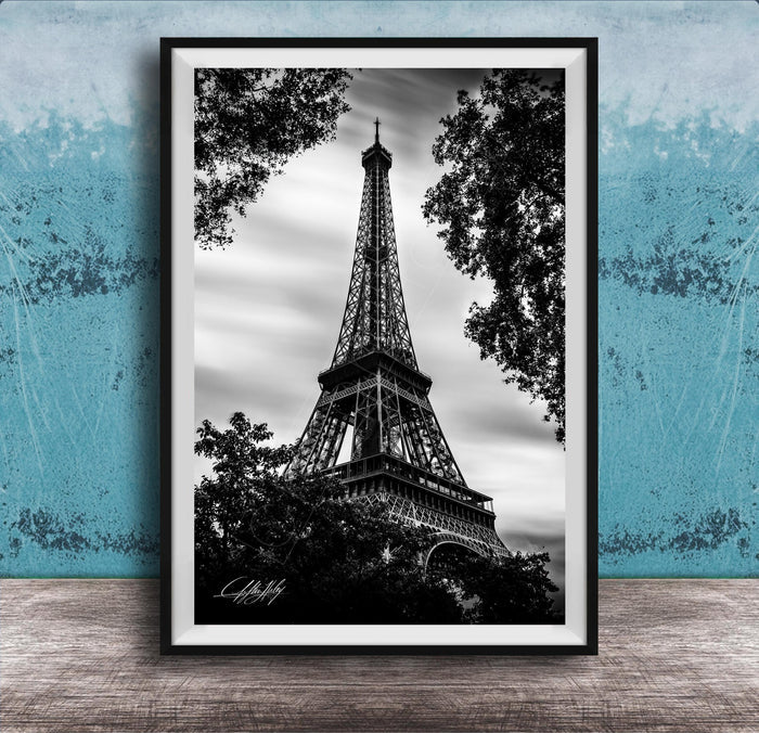 A black and white photograph of the Eiffel Tower, a famous landmark in Paris, France, framed and displayed on a wooden surface against a blue textured background.
