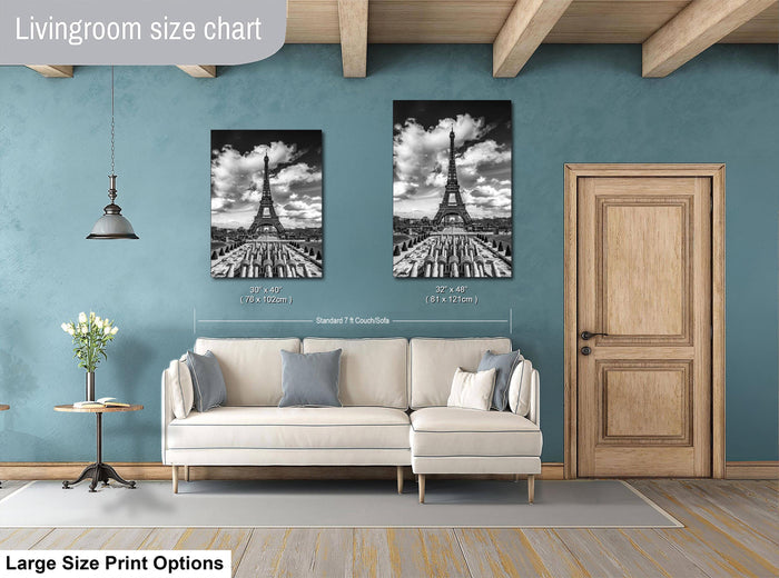 a living room with a white sofa and a wooden door. Above the sofa, there are two framed black and white photographs of the Eiffel Tower. The wall behind the sofa has a blue color, and there is a lamp hanging from the ceiling. The living room appears to be well-decorated and spacious.