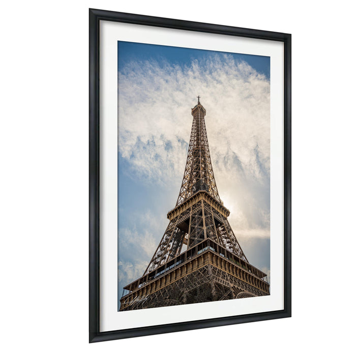 the Eiffel Tower, a famous landmark in Paris, France. The tower is captured from a low angle, emphasizing its height and grandeur against a cloudy sky.