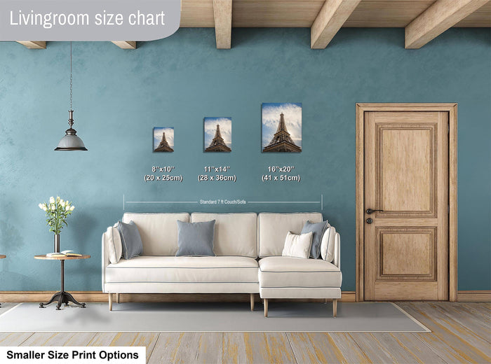 a living room with a white sofa, a wooden door, and a hanging light fixture. There are three framed pictures of the Eiffel Tower displayed on the wall, each with a different size. The living room appears to be well-decorated and spacious.