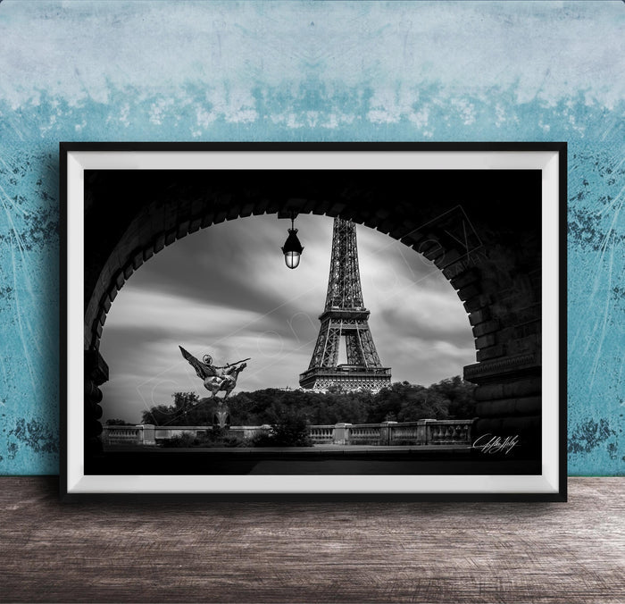 A black and white photograph of the Eiffel Tower in Paris, France, framed and displayed on a wooden surface against a blue textured wall.