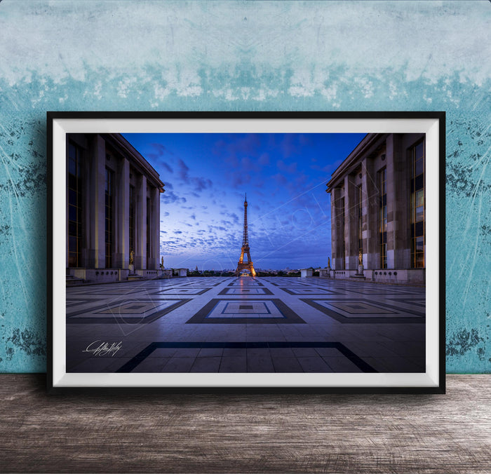 a large, framed photograph of the Eiffel Tower in Paris, France, with the tower illuminated against a blue sky.