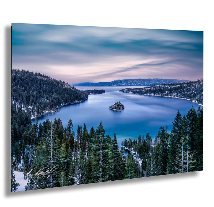 A serene landscape featuring a deep blue lake surrounded by a forested mountain range, with a small island in the center of the lake. The sky is filled with clouds, creating a picturesque and tranquil atmosphere.