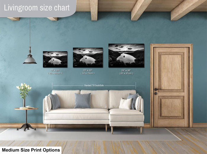 a living room with a white sofa and a wooden door. Above the sofa, there is a livingroom size chart that provides the dimensions of three framed black and white landscape photographs. The chart indicates that the largest photograph is 24 inches wide and the smallest is 18 inches wide. The medium size print options are not described, and the image is not a collage of multiple images.