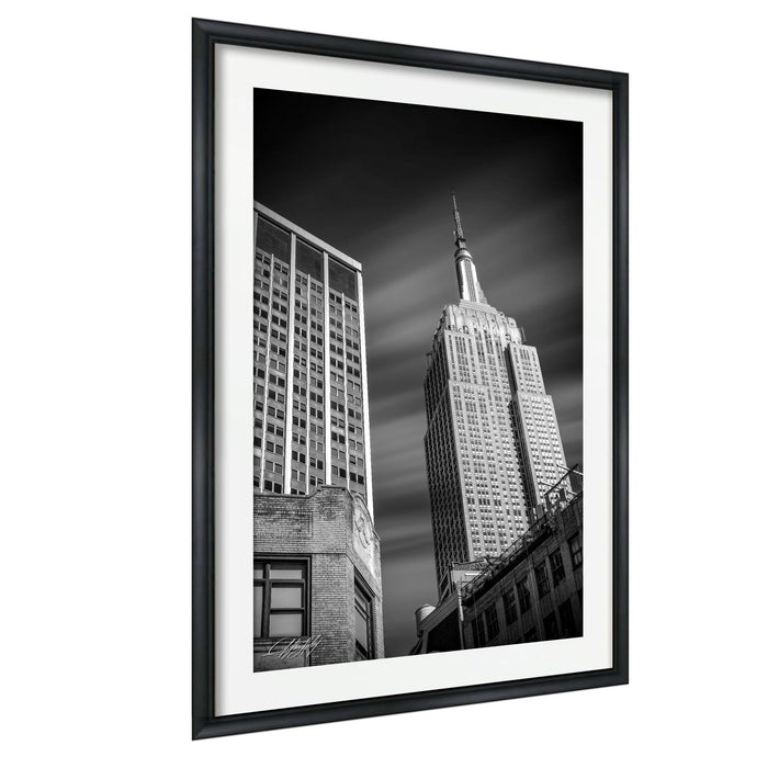 A black and white photograph of the Empire State Building, a famous skyscraper in New York City, captured in a framed black frame.