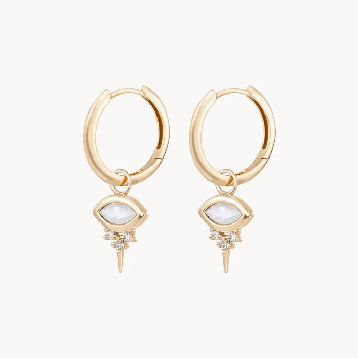 Side view of a pair of evil eye shaped earring charms with marquise-shaped rainbow moonstone at the centre and three small diamonds underneath followed by a small spike at the bottom, hung on gold hoop earrings and displayed on a clean off-white background.