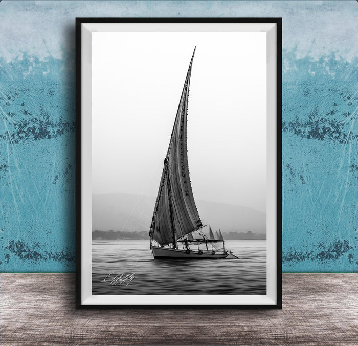 This luxury black and white fine art photograph captures a felucca sail boat drifting along the Nile River at sunset near Luxor, Egypt. Soft fog and minimalist composition create a timeless, monochrome aesthetic rooted in Egyptian river culture. Ideal for collectors and interior designers seeking refined, museum-quality wall art that embodies elegance, simplicity, and enduring calm.
