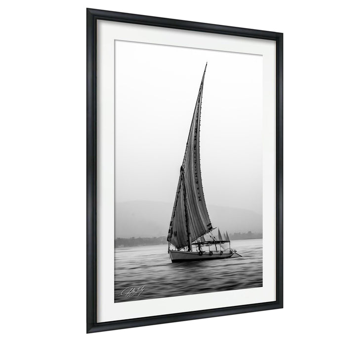 This luxury black and white fine art photograph captures a felucca sail boat drifting along the Nile River at sunset near Luxor, Egypt. Soft fog and minimalist composition create a timeless, monochrome aesthetic rooted in Egyptian river culture. Ideal for collectors and interior designers seeking refined, museum-quality wall art that embodies elegance, simplicity, and enduring calm.