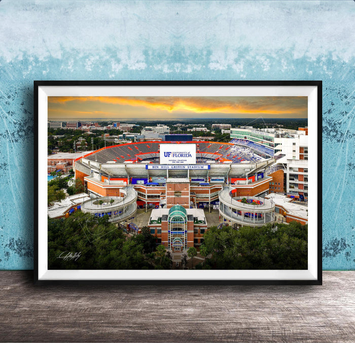 The image is a framed photograph of the Ben Hill Griffin Stadium inUF, Florida, with a sunset sky in the background.
