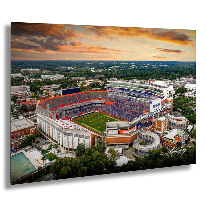 An aerial view of a large sports stadium with a crowd of spectators, surrounded by a cityscape and a colorful sunset sky.