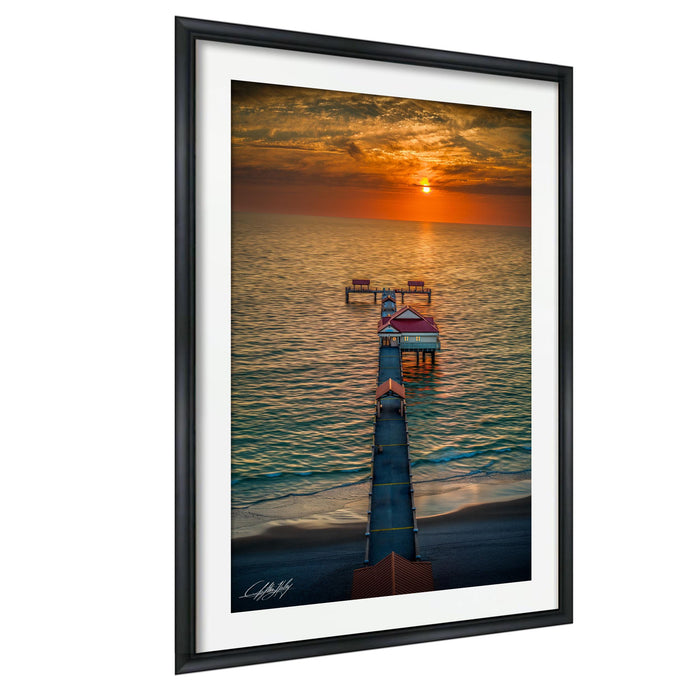 a serene sunset over the ocean, with a pier extending into the water and a small building on the pier.