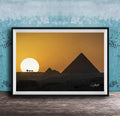 A framed photograph depicting the silhouette of the Great Pyramids of Giza against a vibrant sunset sky, with camels in the foreground.