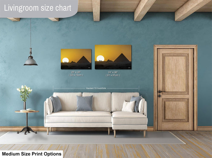 a living room with a white sofa, a wooden door, and a painting of a sunset on the wall. The painting is of two different sizes, with one being larger than the other. The living room appears to be well-decorated and cozy, with a potted plant and a vase adding to the ambiance.