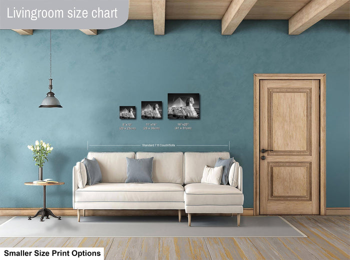 a living room with a white sofa, a wooden door, and a hanging light fixture. There are three framed black and white photographs of buildings displayed on the wall above the sofa.