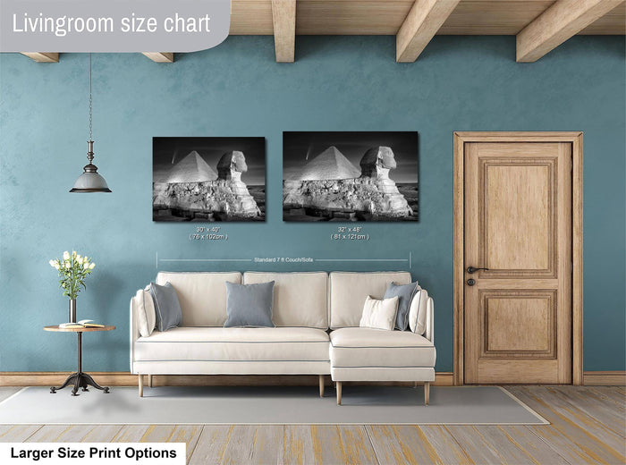 a living room with a white sofa and a wooden door. Above the sofa, there are two framed photographs of the Great Pyramids of Giza, which are the focal point of the room. The living room appears to be designed for comfort and relaxation, with a cozy atmosphere created by the furniture and the large size of the photographs.