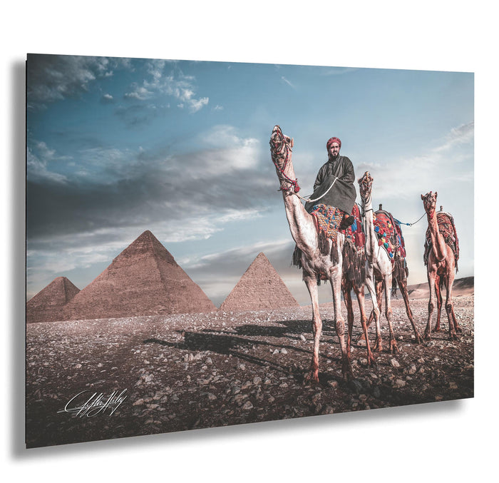 A man rides a camel in front of the iconic pyramids of Giza, Egypt, with a cloudy sky in the background.
