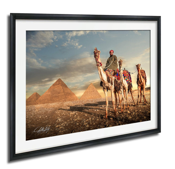 A man rides a camel in front of the iconic pyramids of Giza, Egypt, with the sun setting in the background.