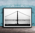 A black and white photograph of the Golden Gate Bridge in San Francisco, California, with a blue textured wall in the background.