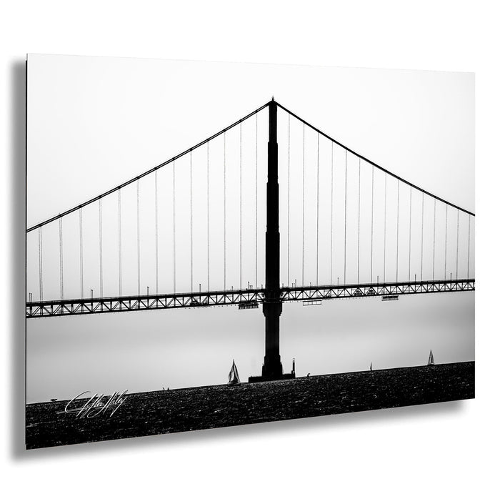 A black and white photograph of a suspension bridge with a long, curved deck and tall, slender towers.
