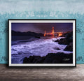 A framed photograph of the Golden Gate Bridge at night, with the bridge illuminated and its towers glowing against the dark sky. The waves are crashing against the rocky shoreline, creating a dramatic and serene scene.