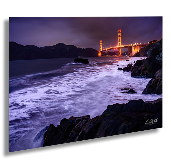 a serene night scene of the Golden Gate Bridge, with its iconic towers illuminated against the dark sky and the waves crashing against the rocky shoreline.