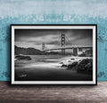 A black and white photograph of the Golden Gate Bridge in San Francisco, California, with the bridge's towers and suspension cables prominently featured against a cloudy sky.