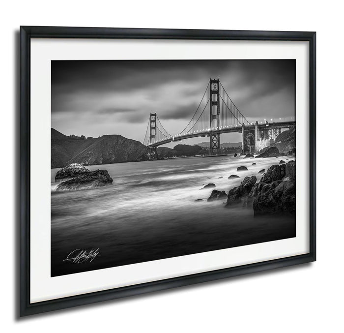 A black and white photograph of the Golden Gate Bridge in San Francisco, California, with the bridge's distinctive towers and suspension cables spanning the bay.