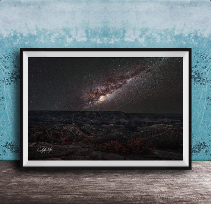 The image is a framed photograph of a night sky with a galaxy, placed on a wooden surface against a blue wall.