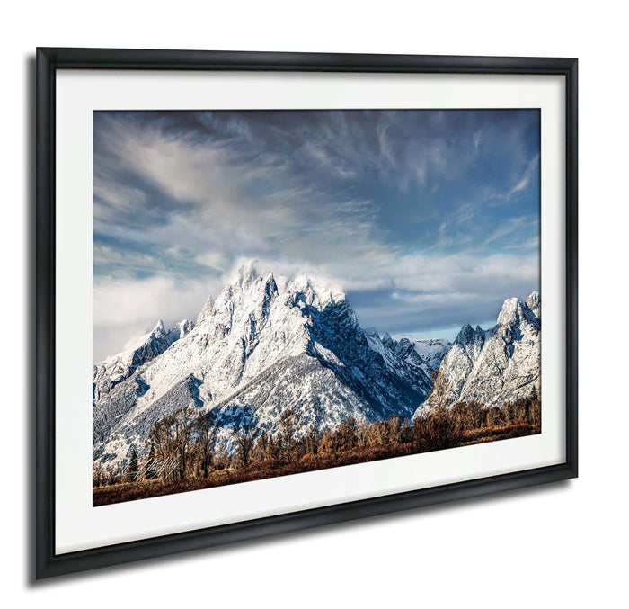 A framed photograph of a snow-capped mountain range against a cloudy sky.