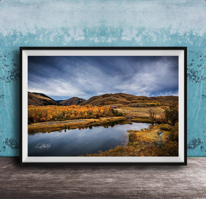 The image is a framed photograph depicting a serene landscape with a lake, mountains, and trees in autumn colors.