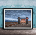 A framed photograph of a sign for Grand Teton National Park, with a cloudy sky and mountains in the background.