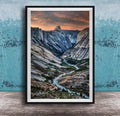 The image is a framed photograph of a mountainous landscape with a winding river, set against a backdrop of a dramatic sky with clouds and a sunset.