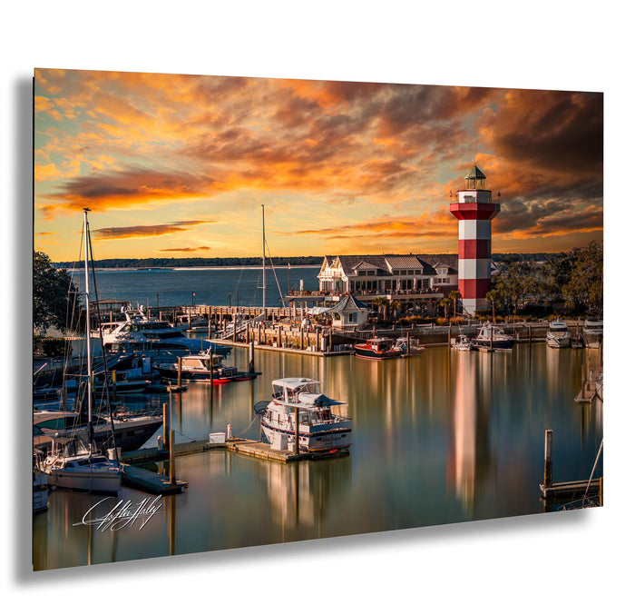 a serene harbor scene at sunset, with boats docked in the calm waters and a lighthouse standing tall in the background. The sky is filled with vibrant orange and pink hues, creating a picturesque and tranquil atmosphere.