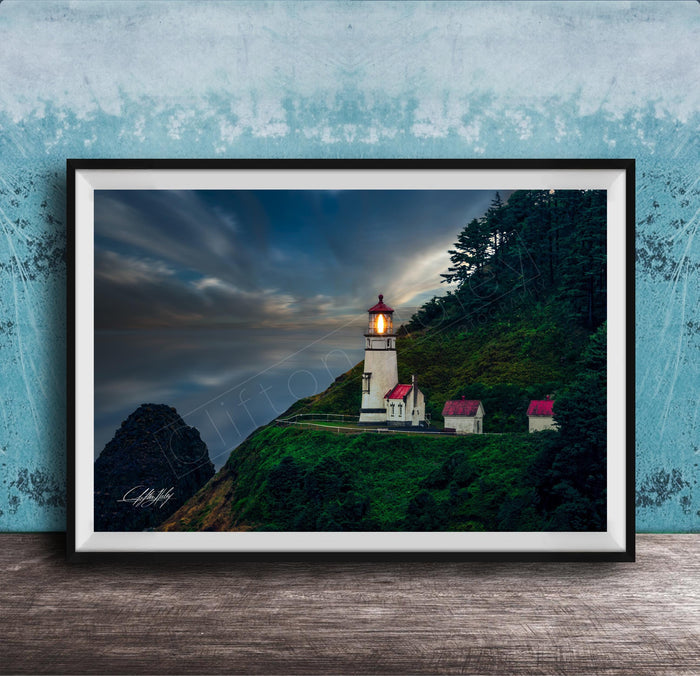 A framed photograph of a lighthouse on a cliff, with a dramatic sky and a small village in the background.
