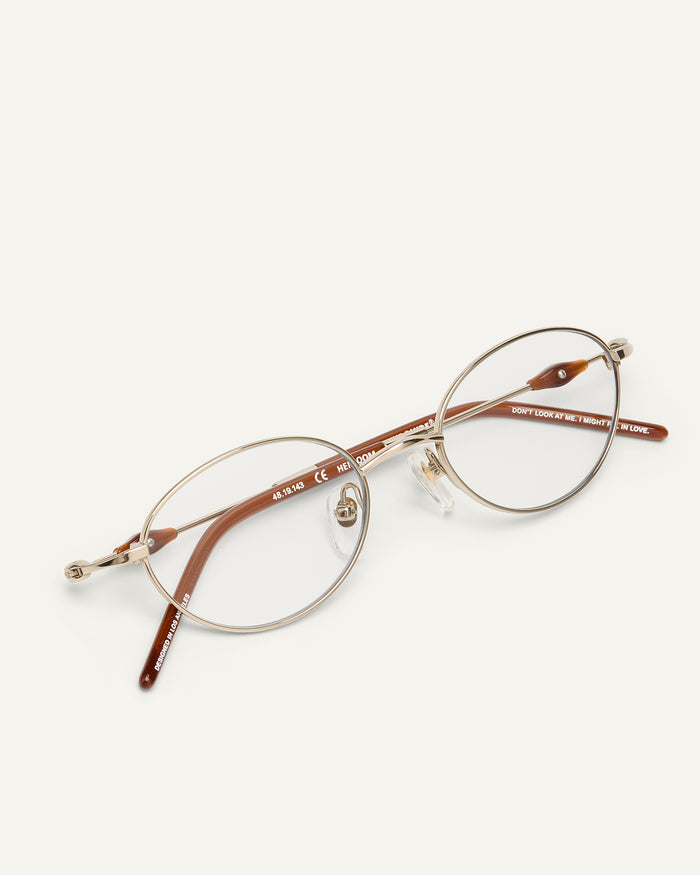 Detail shot of Bonnie Clyde Heirloom optical frames in gold and dark brown with clear lenses.