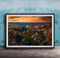 The image is a framed aerial view of a harbor with boats docked, set against a backdrop of a colorful sunset sky.